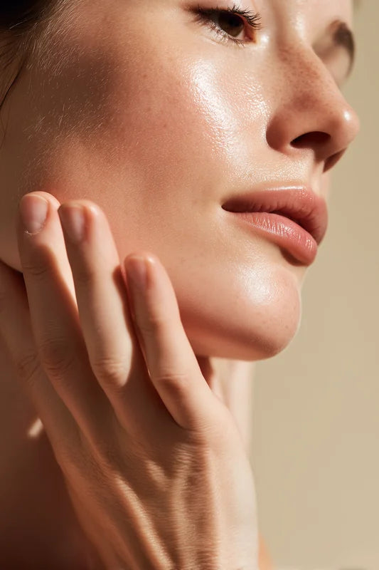 Close-up of a person's face with a hand gently touching the cheek, against a neutral background.